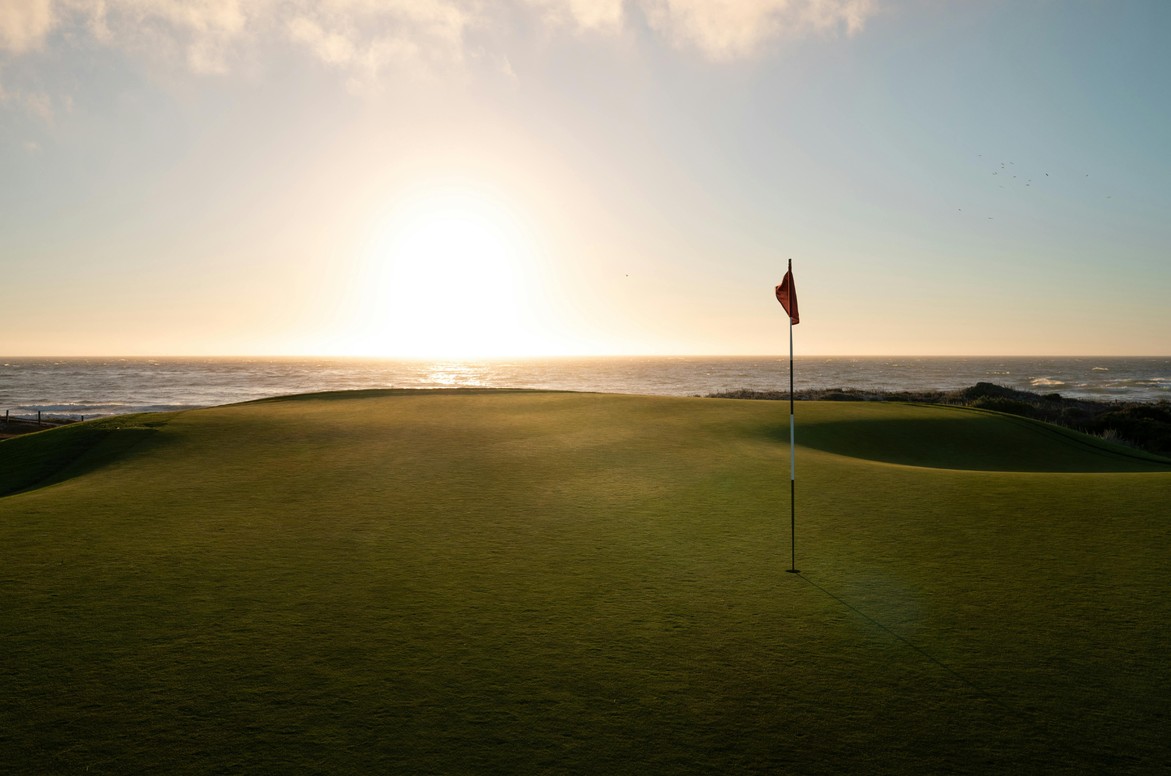 A golf green and flag at sunset over the sea